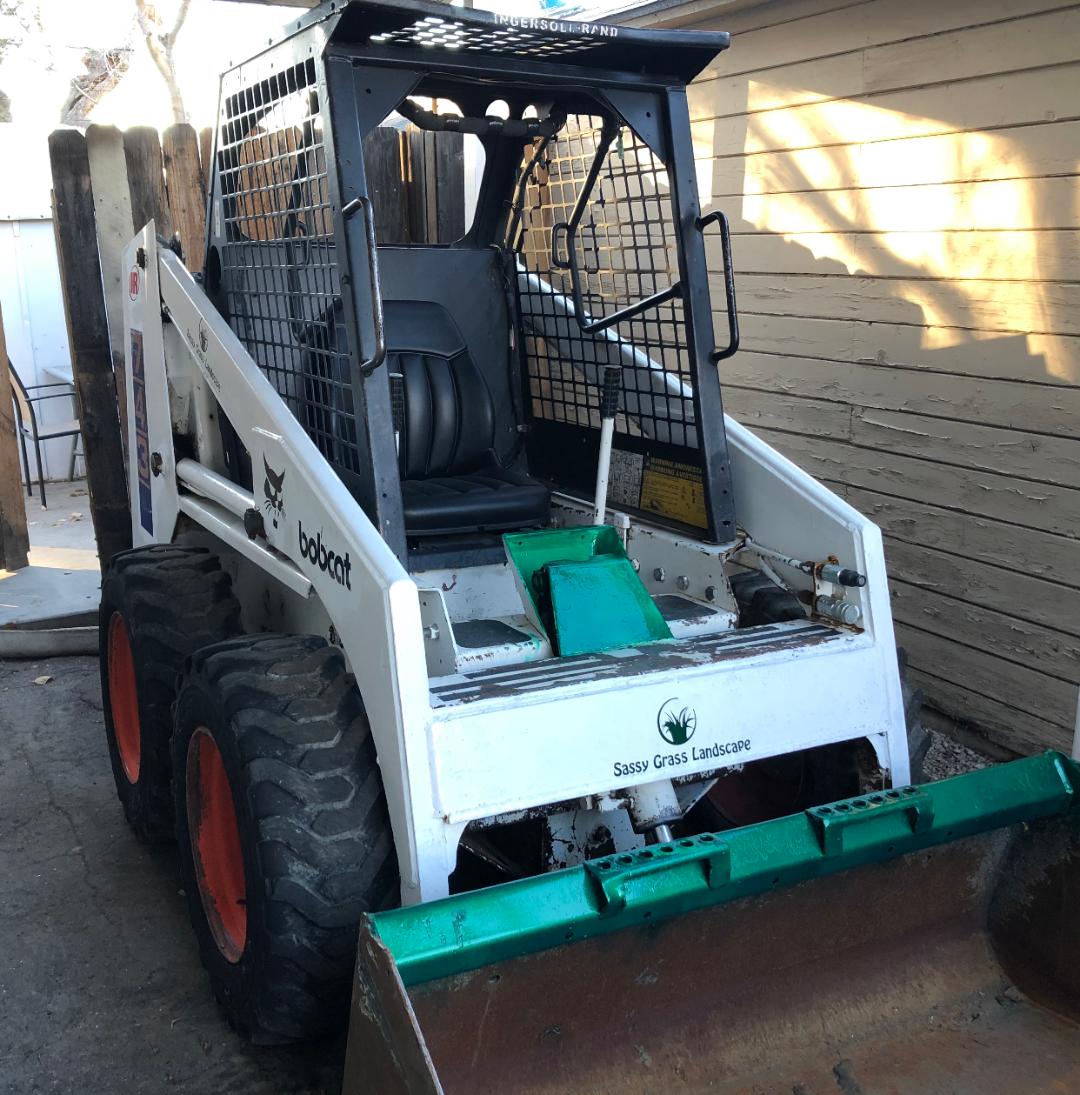 a bobcat skidsteer for earth moving. Has the Logo for Sassy Grass Landscape and a green painted bucket attachment
