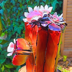 Decorative metal flower sculpture with red and pink flowers against a green outdoor background