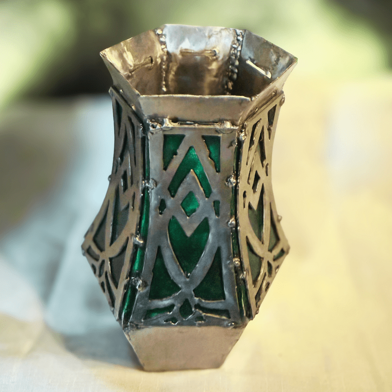 Decorative vase with green glassy features and silver metalwork on a blurred background