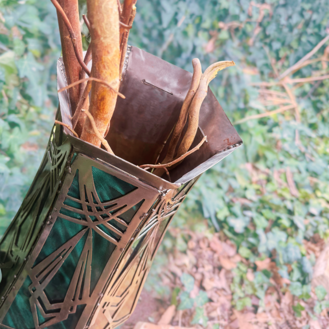 Decorative metal vase with intricate designs and branches on a blurred natural background