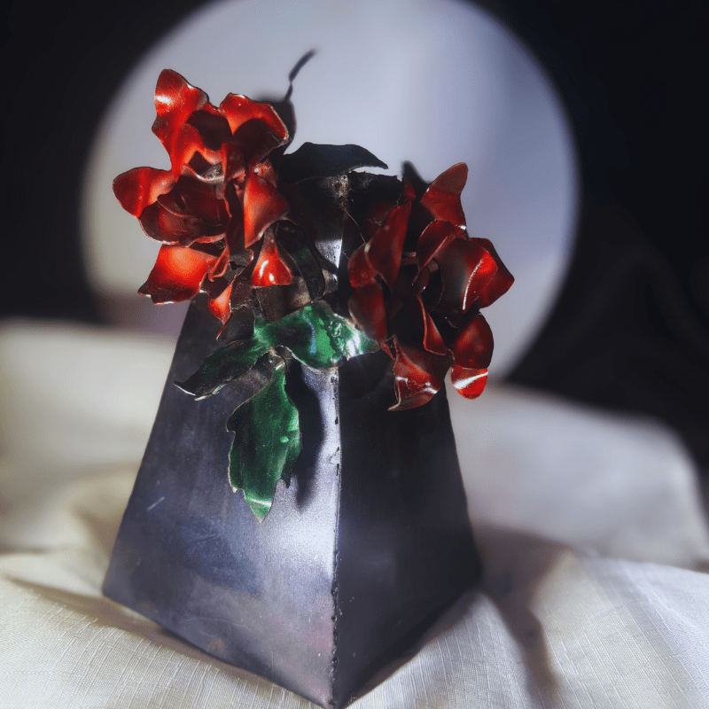 Decorative vase with red flowers and green leaves on a textured surface