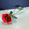 Red rose-shaped object with green leaves on a white surface