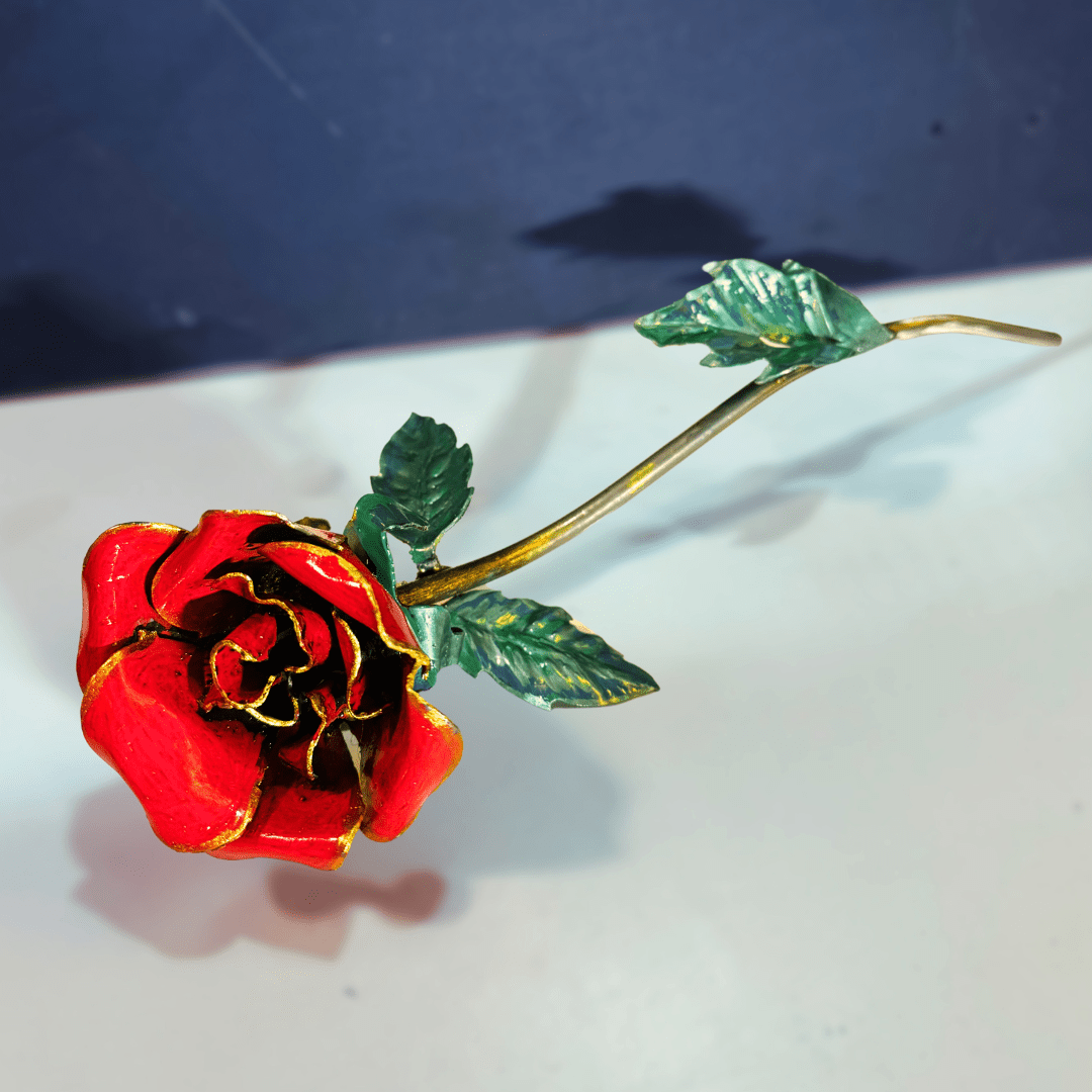 Red rose-shaped object with green leaves on a white surface