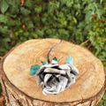 Metallic rose with green leaves, bronze and gold accents on a wooden stump with green foliage in the background