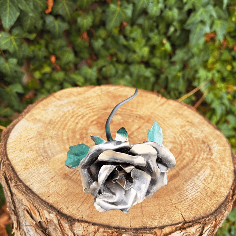 Metallic rose with green leaves, bronze and gold accents on a wooden stump with green foliage in the background