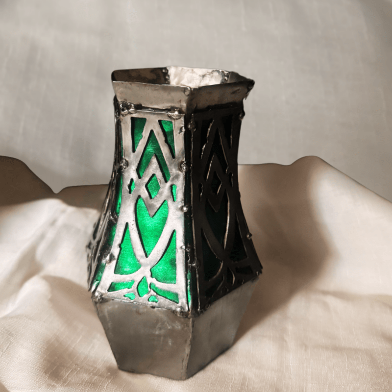 Metal Geometric vase with silver and green metallic colors, on a cloth background