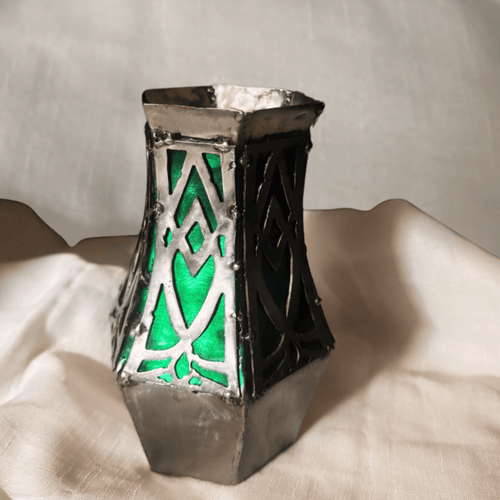 Metal Geometric vase with silver and green metallic colors, on a cloth background