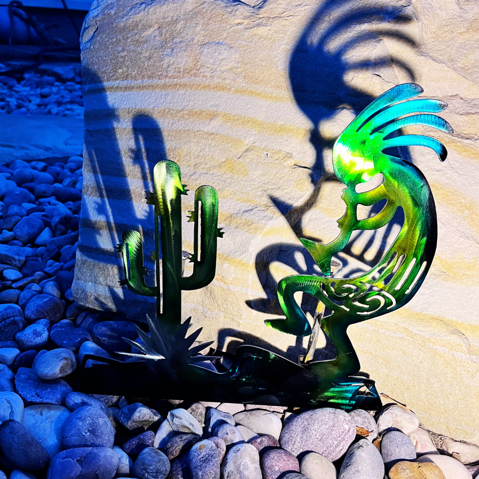 kokopelli figure and cactus displaying a shadow on the rock behind. In a natural landscape with cobble rocks