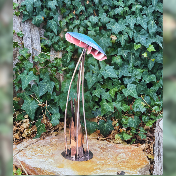 Metallic sculpture with pink top on a stone surface against a green ivy background